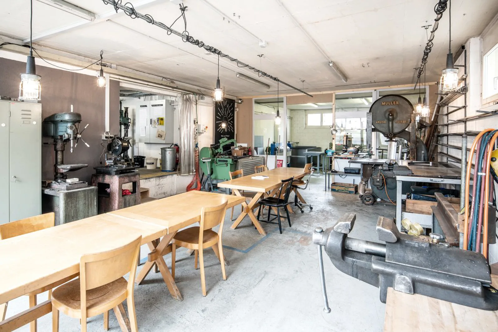 Blick in die Werkstatt der Buitig: langer Holztisch mit Stühlen, dahinter Ständerbohrmaschine und weitere Maschinen